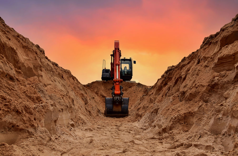 Excavator in sandy trench at sunset